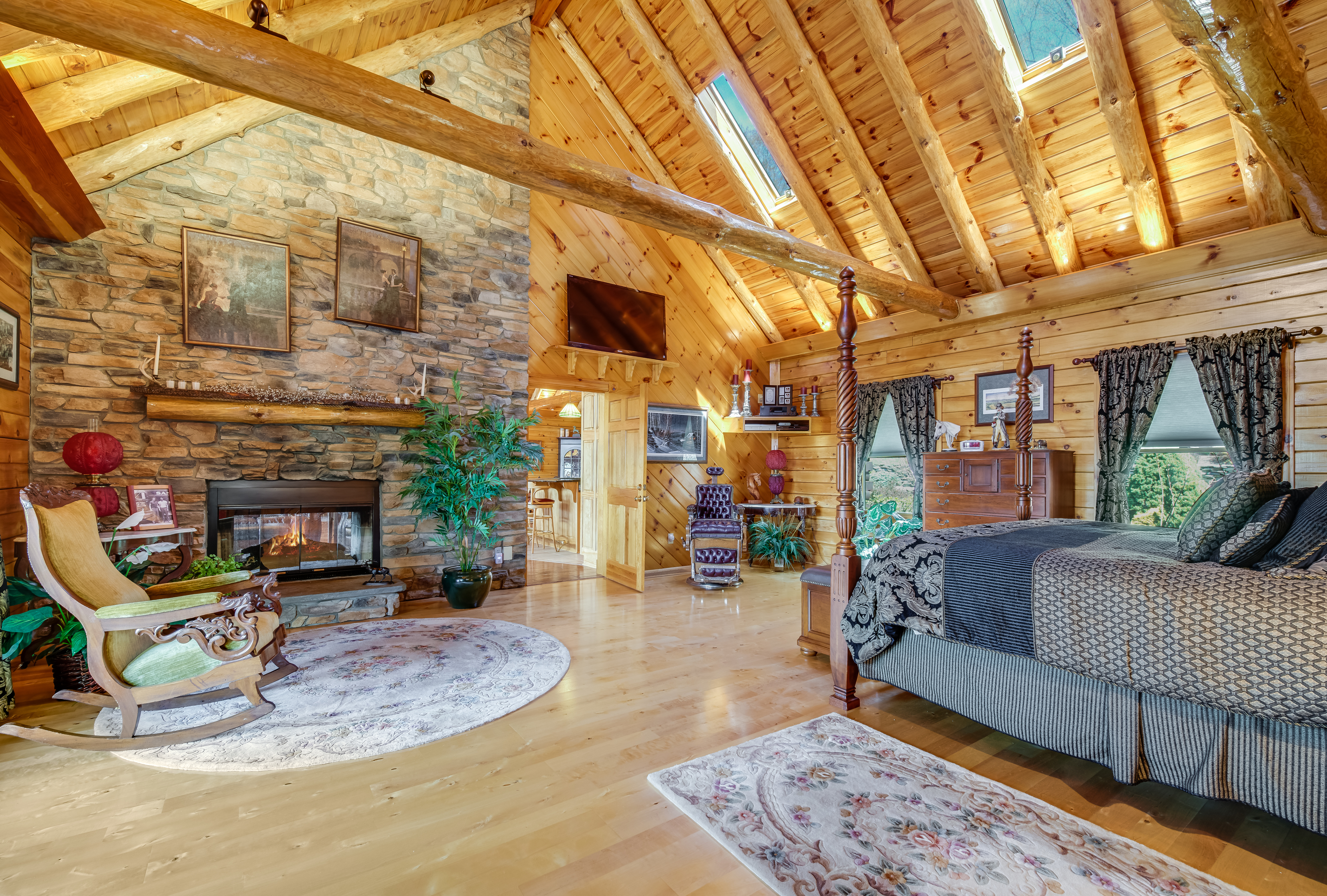 A cozy log cabin bedroom with a vaulted wood ceiling, stone fireplace, large bed, and wooden furniture offers rustic warmth—perfect for Charleston rental marketing seeking inviting, memorable spaces.